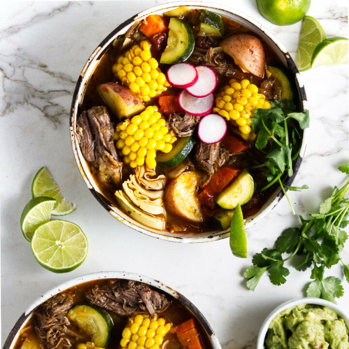 A large bowl of Mexican beef soup with vegetables and garnished with cilantro and limes.
