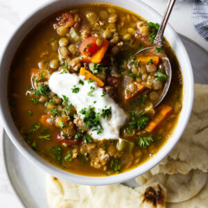 A bowl of lentil turkey soup next to pieces of pita bread.