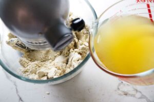 Pouring chicken broth into the mixture in a mixing bowl.