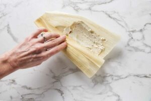 Wrapping masa corn dough into a corn husk.
