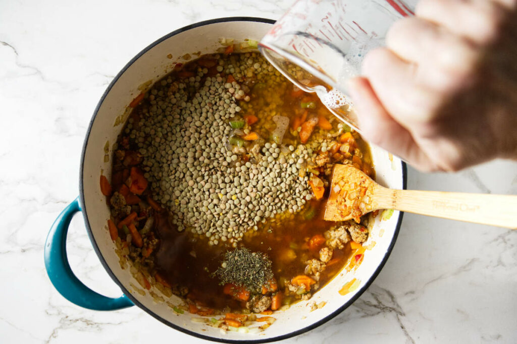 Adding broth to a pot of soup.