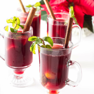 Tall cups of hat Ponche garnished with cinnamon sticks and fresh mint sprigs.