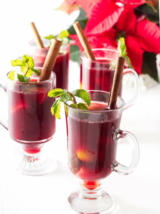 Tall cups of hat Ponche garnished with cinnamon sticks and fresh mint sprigs.