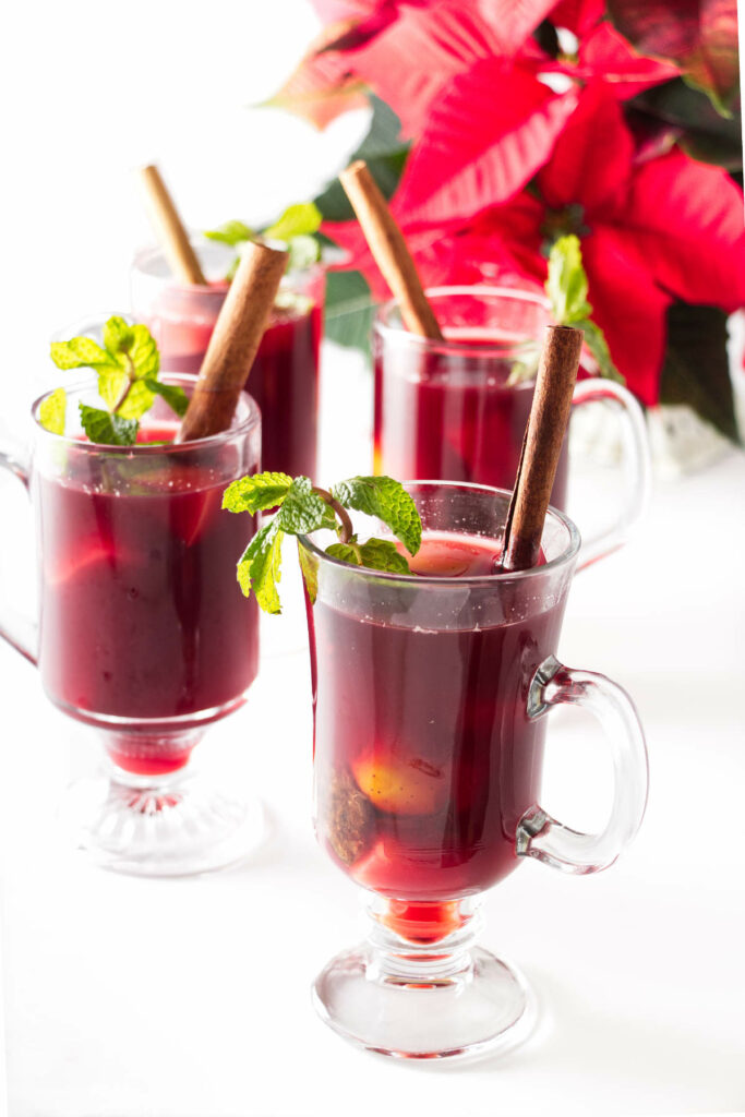 Tall cups of hat Ponche garnished with cinnamon sticks and fresh mint sprigs.