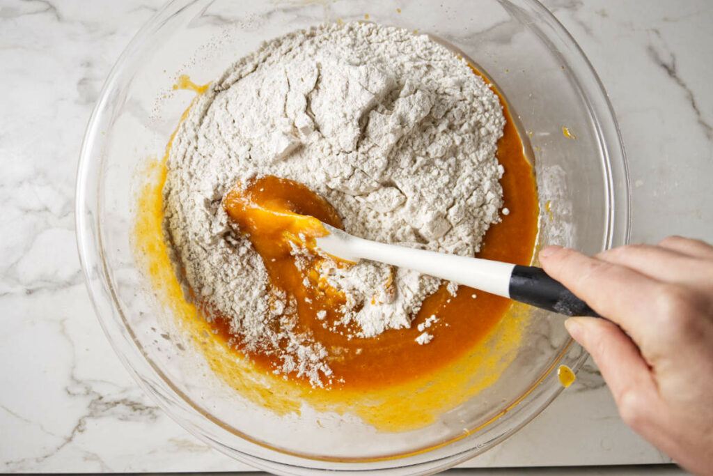 Stirring flour into pumpkin batter.