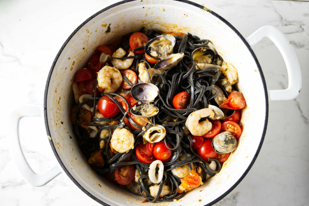Adding the clams and squid ink pasta to the pot.