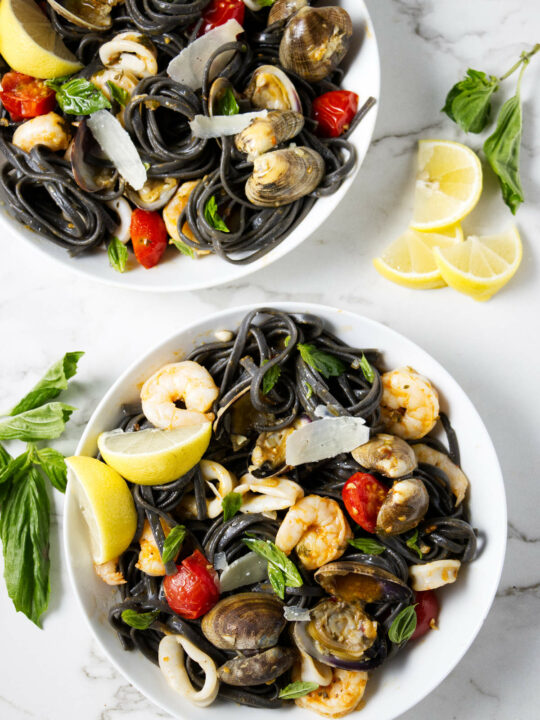 Two servings of squid ink pasta with seafood.