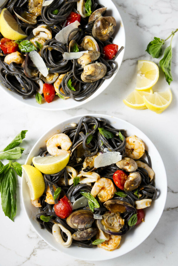 Two servings of squid ink pasta with seafood.