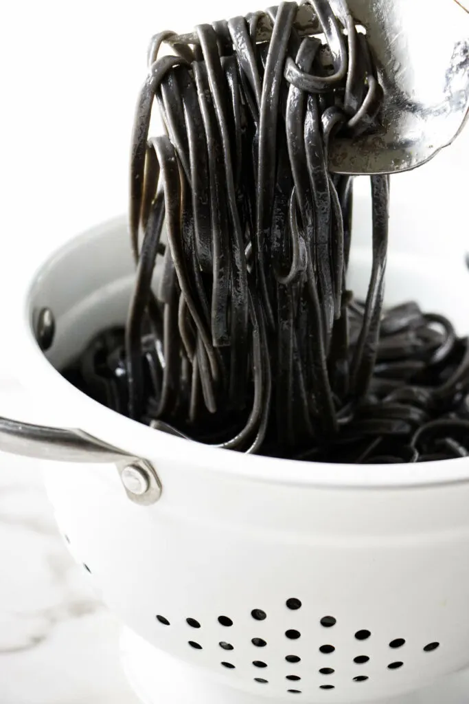 Freshly cooked squid ink pasta in a colander.
