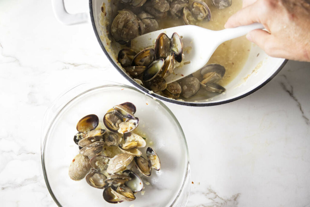 Placing cooked clams in a bowl.