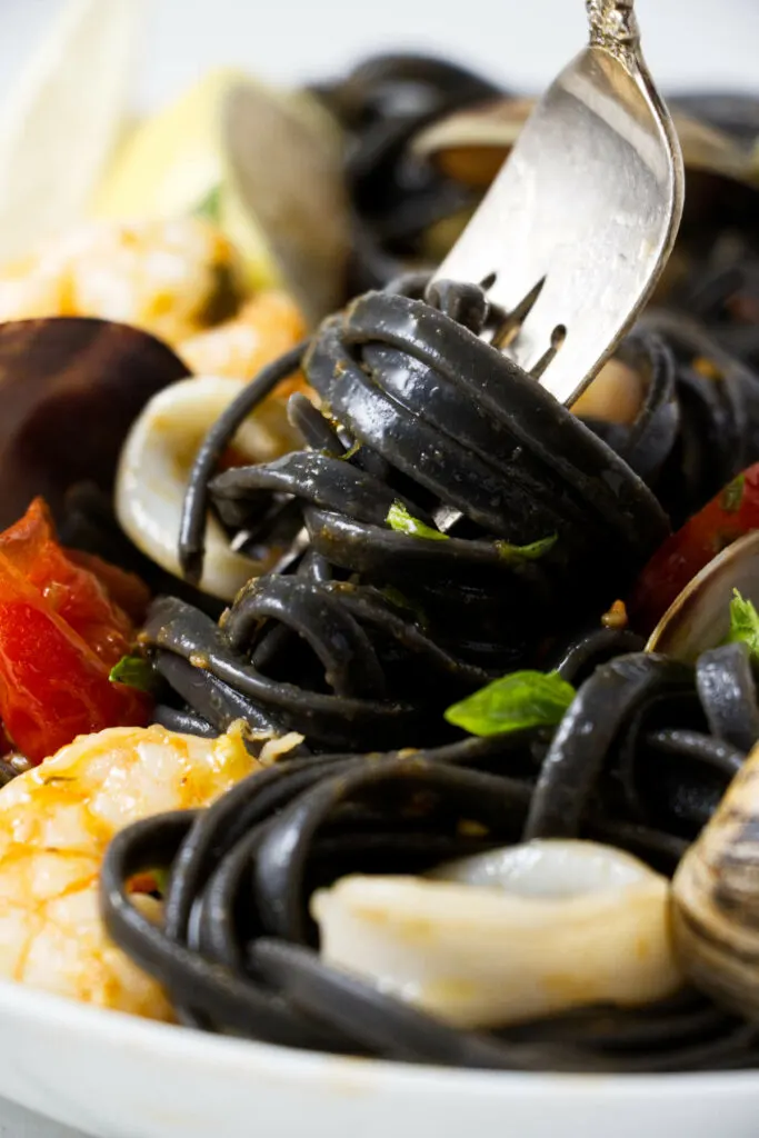 Black pasta wrapped around a fork next to seafood.