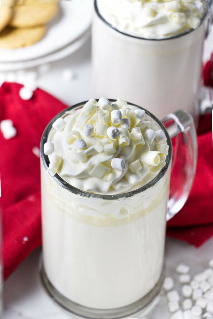 Two mugs of white hot chocolate topped with whipped cream.