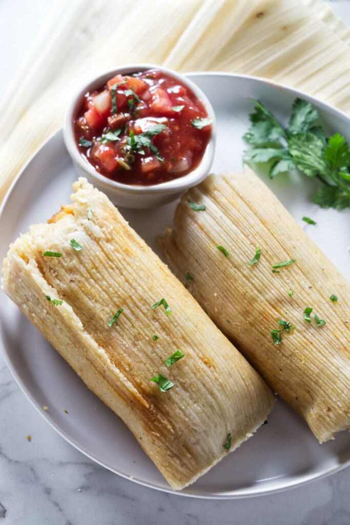 Two tamales on a plate with salsa.