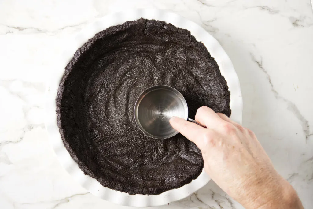 Pressing chocolate cookie crumbs in the bottom of a pie dish.