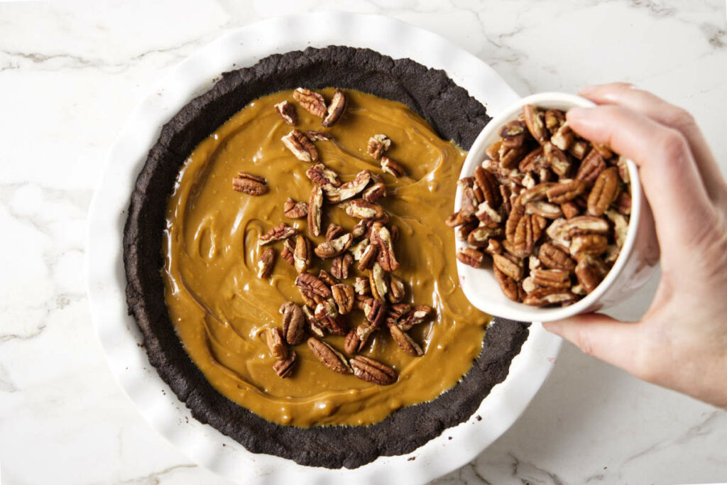 Adding caramel sauce and pecans on top of the pie crust.