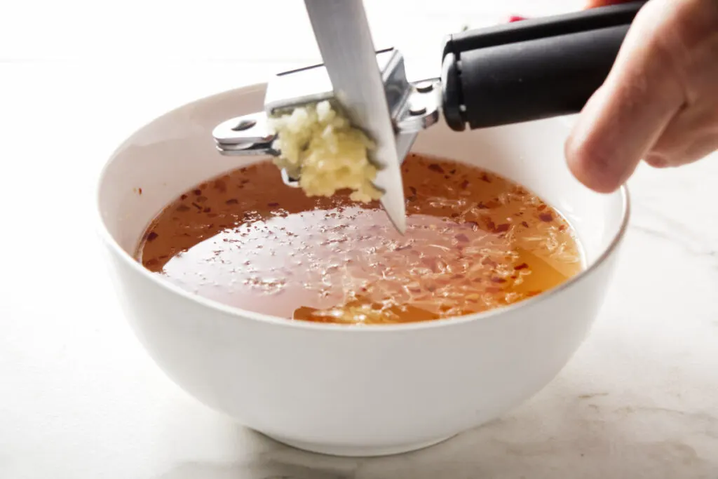 Crushing garlic cloves and mixing it into a bowl of sauce.