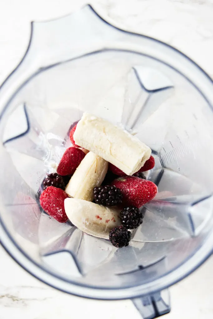 Adding frozen fruit to a blender.