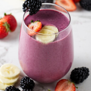 A fruit smoothie topped with slices of banana, strawberry, and blackberries.