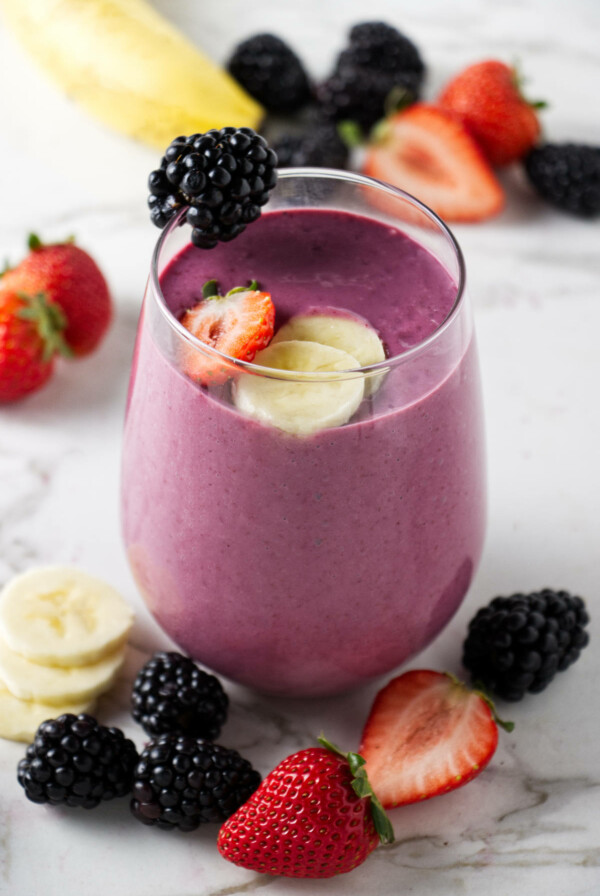 A fruit smoothie topped with slices of banana, strawberry, and blackberries.