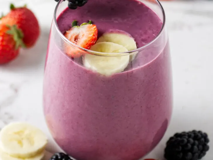 A fruit smoothie topped with slices of banana, strawberry, and blackberries.