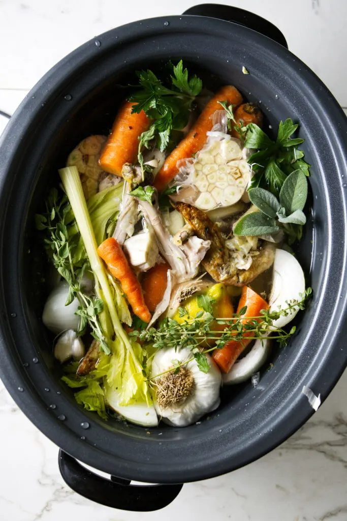 A slow cooker with vegetable scraps and chicken bones.