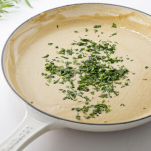 Close up view of a skillet of lobster sauce with chopped tarragon.