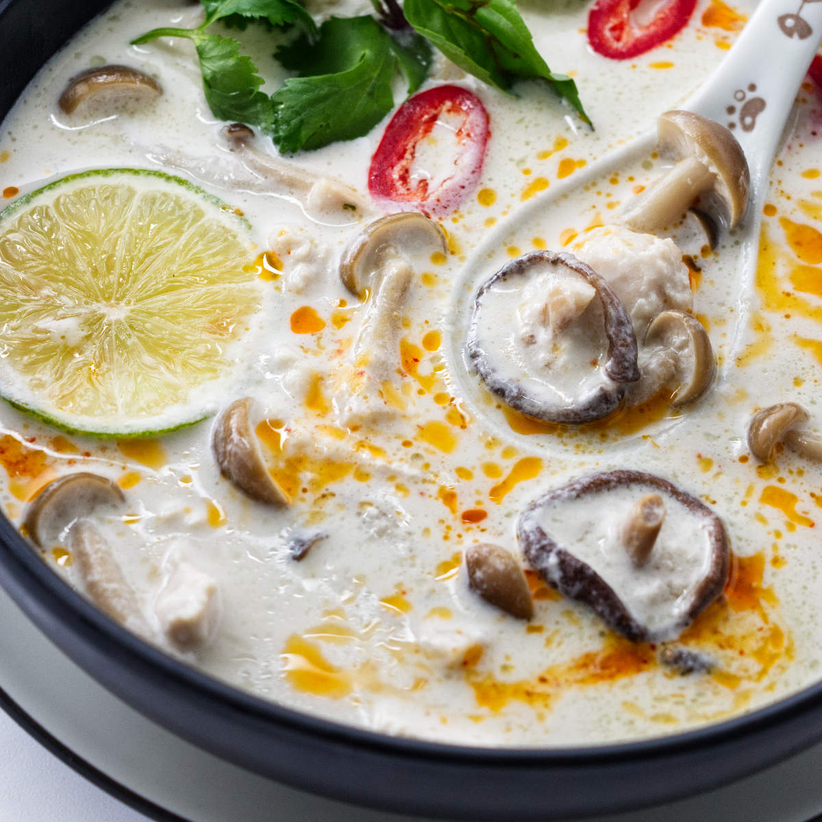 a close up of a serving Tom Kha Soup garnished with chili oil and fresh Thai basil.