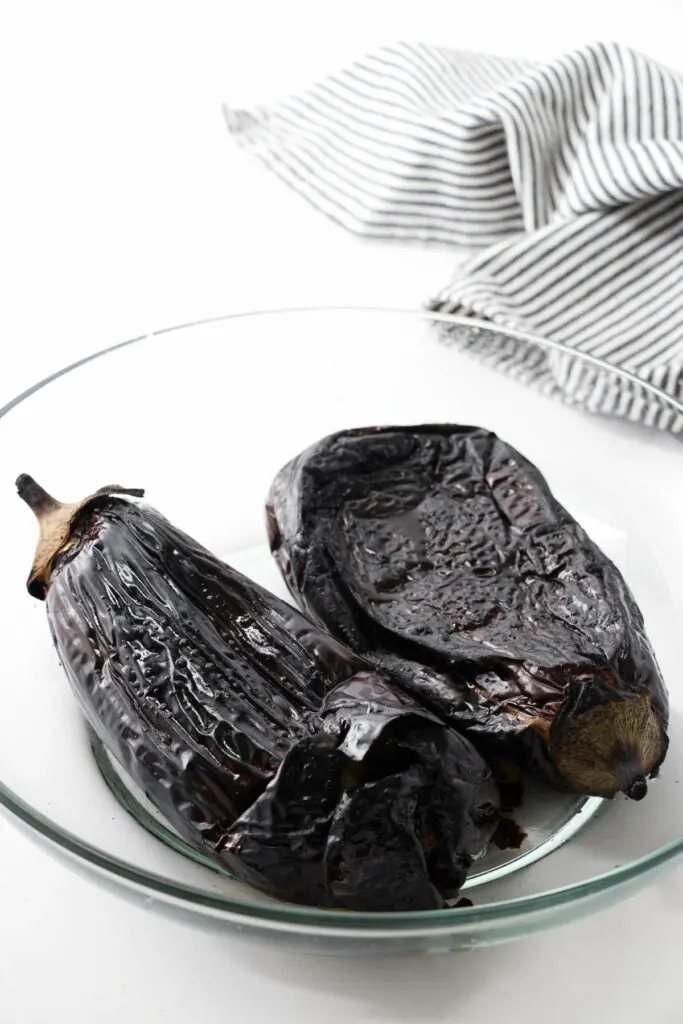 Placing roasted eggplant in a bowl to let them steam.