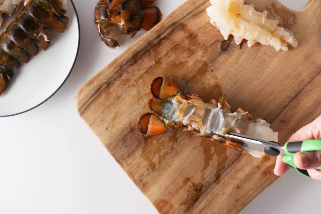 Cutting board with scissors cutting the shell from a lobster tail