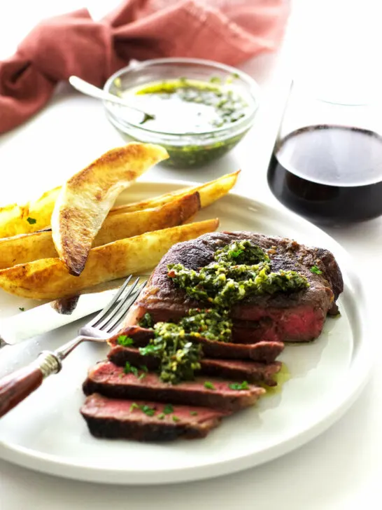 A steak with chimichurri sauce and potato wedges.