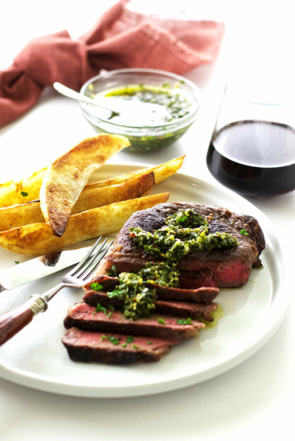 A steak with chimichurri sauce and potato wedges.