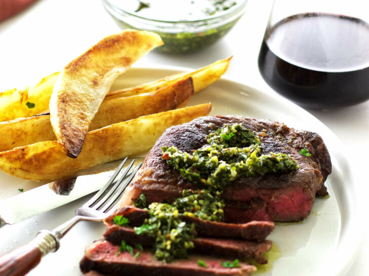 A steak with chimichurri sauce and potato wedges.