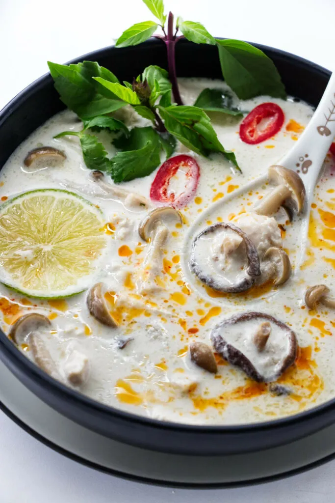 a bowl of Tom Kha Soup garnished with chili oil and fresh Thai basil.