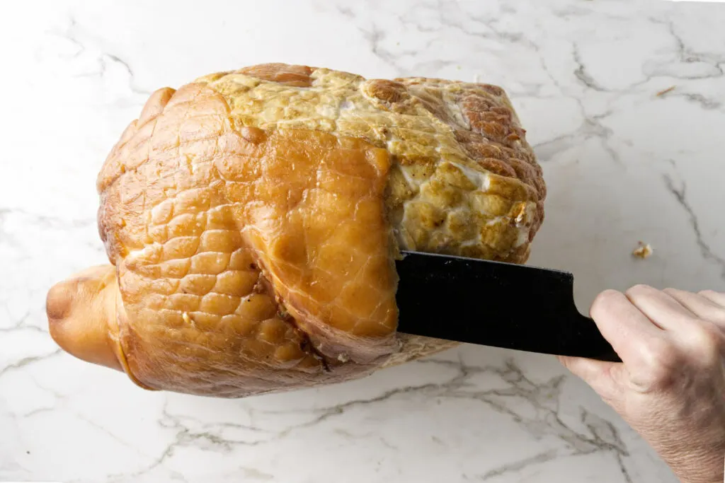 Sliding a knife under the rind of a ham.