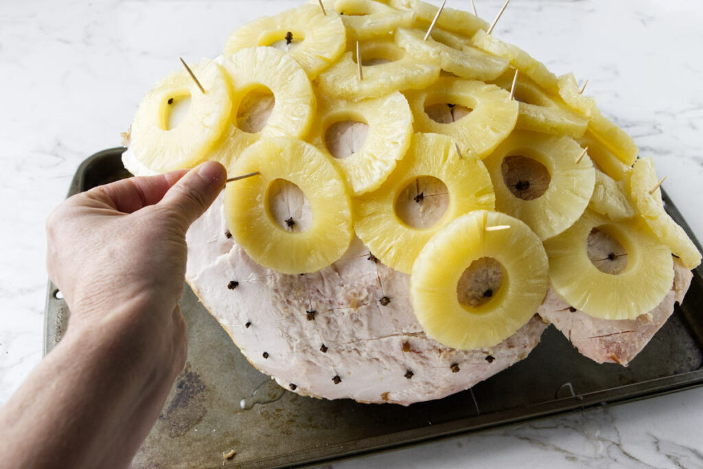 Using toothpicks to stick pineapple rings on a ham.
