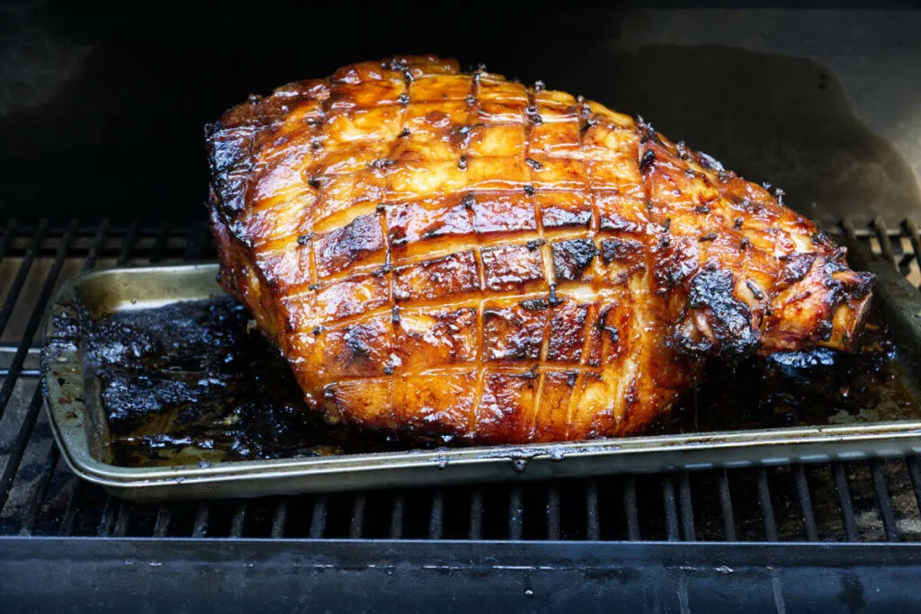 A glazed ham on the grill of a Traeger.