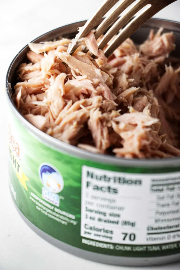A fork fluffing tuna in a can.