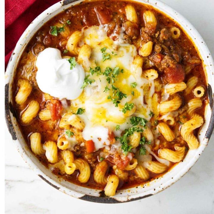 A bowl of crockpot goulash topped with cheese and sour cream.