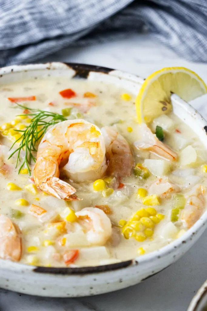 A bowl of soup with a shrimp and dill on top.