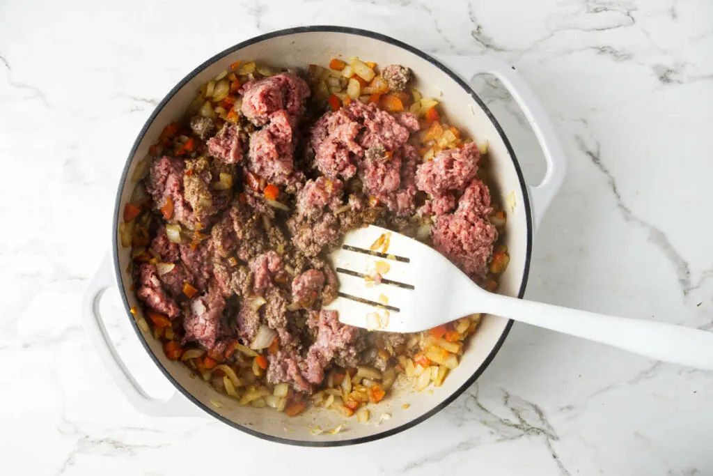 Adding ground beef to the skillet.