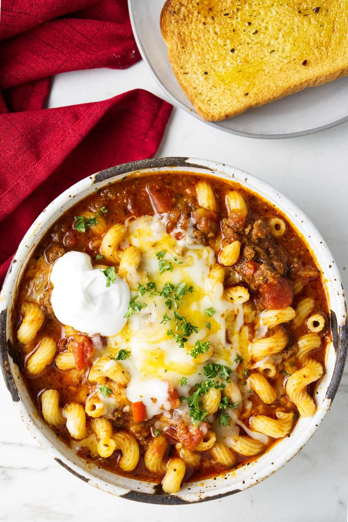 A bowl of American goulash next to a slice of Texas toast.
