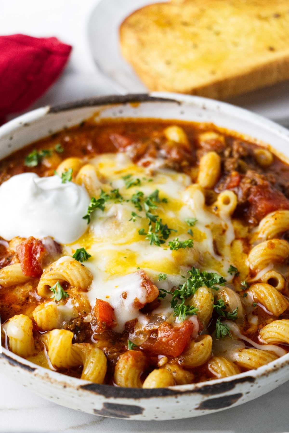 Ground beef and pasta goulash in a bowl with cheese and sour cream.