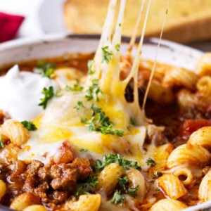 A spoon scooping cheese and pasta from a dish.