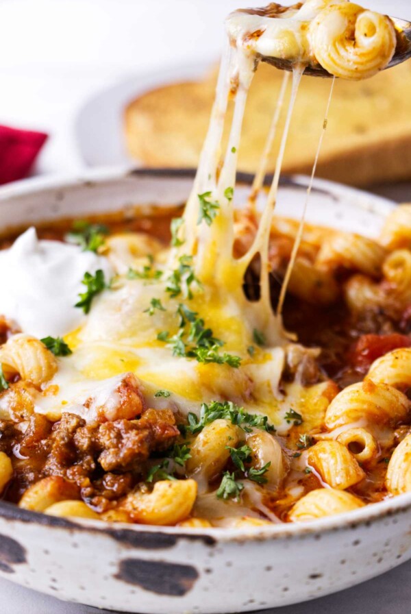 A spoon scooping cheese and pasta from a dish.