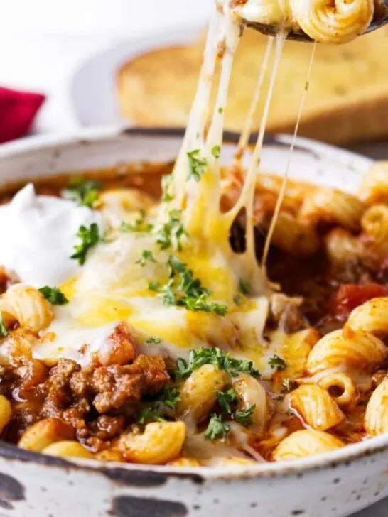 A spoon scooping cheese and pasta from a dish.