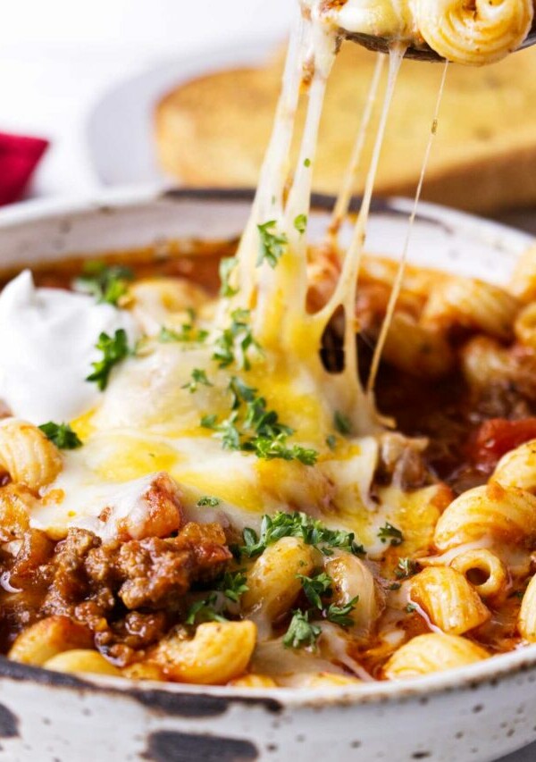 A spoon scooping cheese and pasta from a dish.