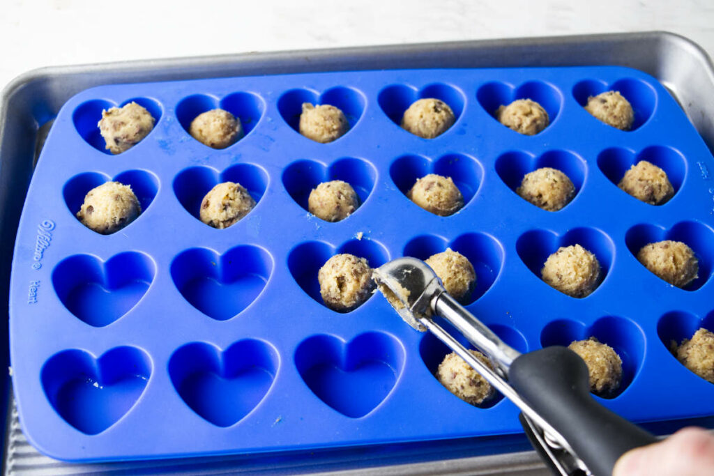 Dropping chocolate chip cookie dough into heart shaped molds.