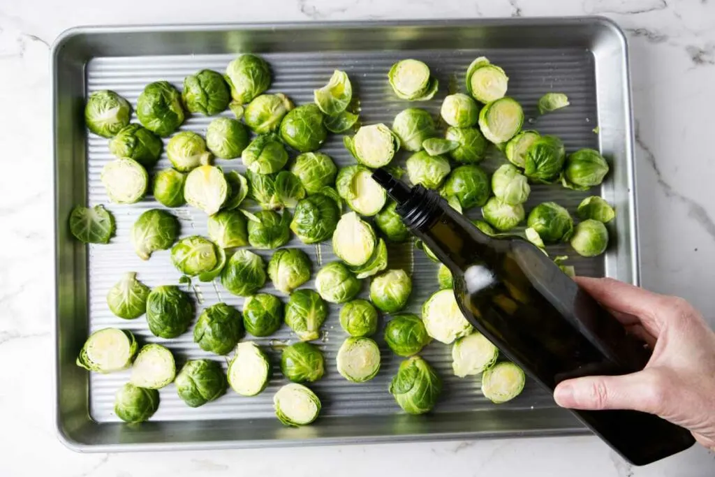 Drizzling olive oil over Brussels sprouts.