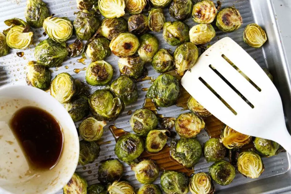 Drizzling honey sriracha sauce over Brussel sprouts on a sheet pan.