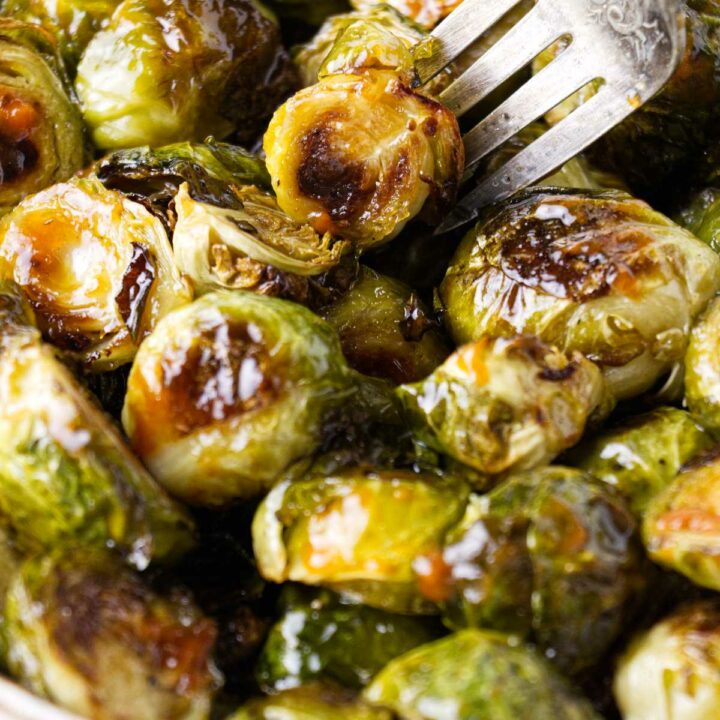 A fork in a dish with honey sriracha brussel sprouts.